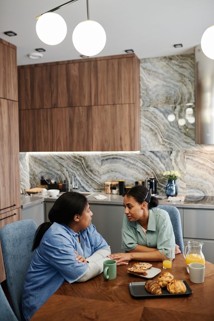 Two women sharing a conversation over breakfast in a modern kitchen setting.